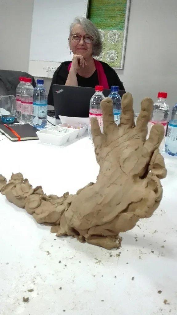 Barbara Schreiner at a craftivism workshop table with a sculpted clay hand