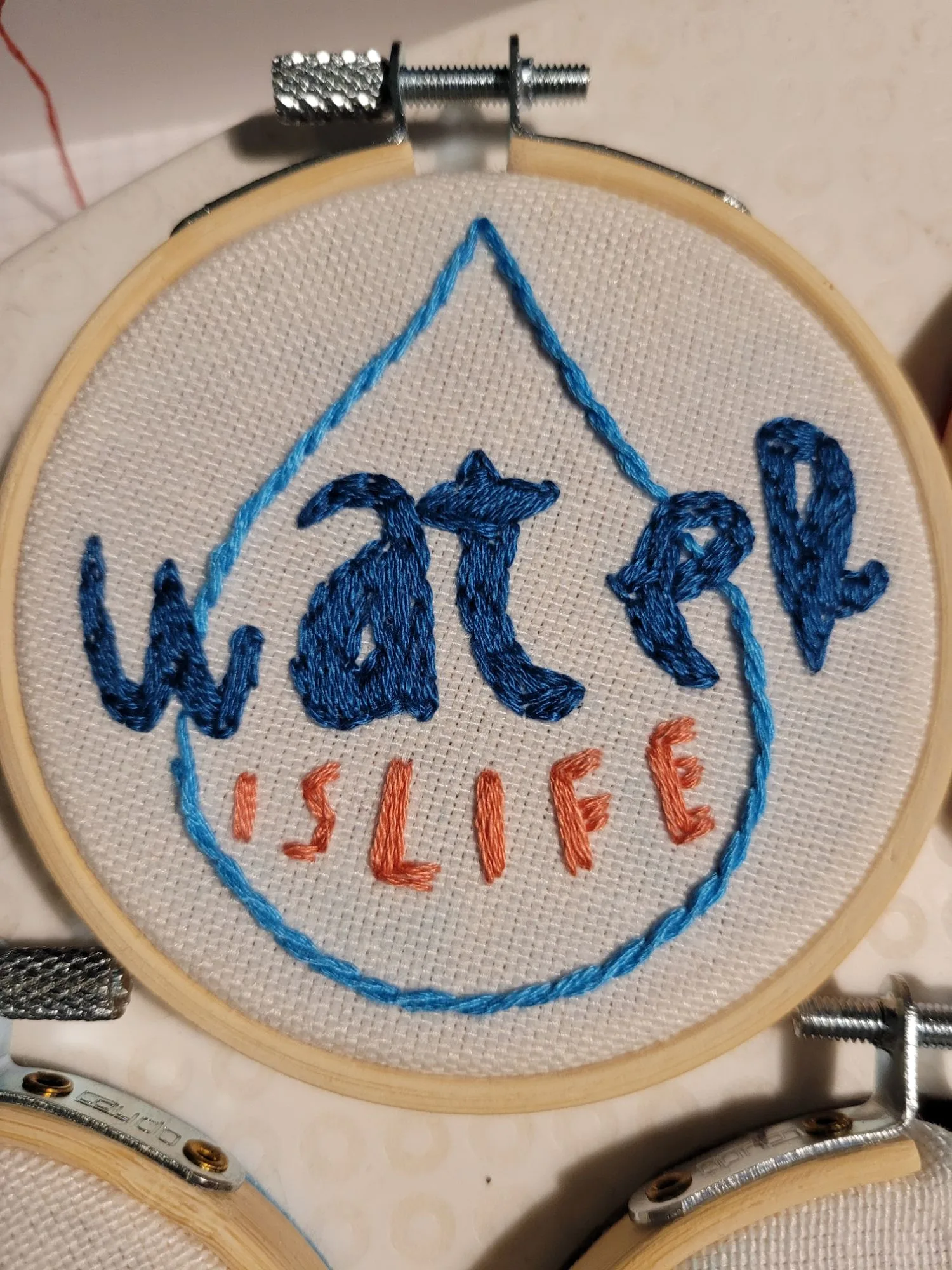 Hand-embroidered hoop reading “Water is Life,” bridging Red Thread’s craft and water justice practices